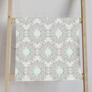 May include: White towel with a repeating pattern of green leaves and red berries arranged in a circular design. The towel is hanging on a wooden ladder in a bathroom setting.