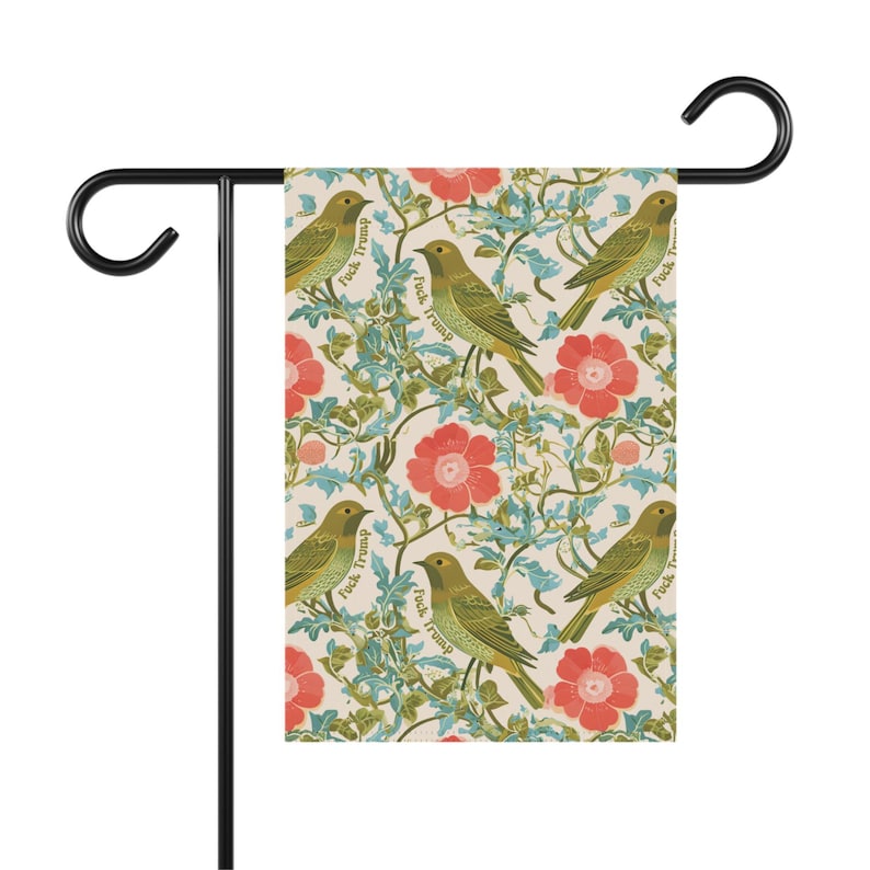 May include: A garden flag featuring a repeating pattern of green birds, red flowers, and green vines on a cream background. The words "Fuck Trump" are printed on the birds. The flag is attached to a black metal stand.