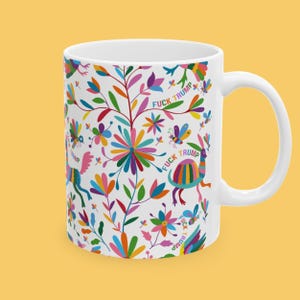 May include: White ceramic mug with a colorful floral and animal pattern. The design includes various flowers, butterflies, and creatures in shades of pink, blue, green, and orange. The text "FUCK TRUMP" is repeated throughout the design.