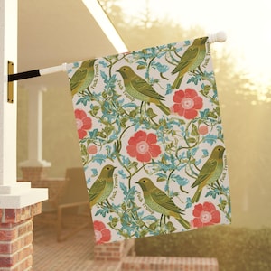 May include: A decorative outdoor flag featuring a repeating pattern of green birds, red flowers, and teal vines on a white background. The phrase "Fuck Trump" is printed on the flag. The flag is mounted on a white pole.
