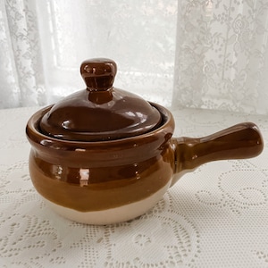 May include: A brown ceramic pot with a lid and a handle. The pot has a white glaze on the bottom half.