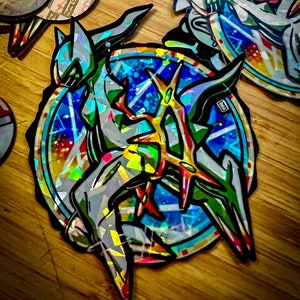 May include: A holographic sticker featuring a colorful, abstract design of a creature with sharp points and a blue, starry background.