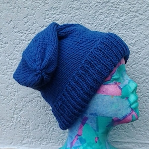May include: A blue knitted beanie with a unique folded design on top. The beanie is made of a soft, textured yarn and is perfect for keeping warm in the winter.