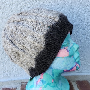 May include: A gray and black knitted beanie with a slouchy fit. The beanie is made of a soft, textured yarn and has a black brim.