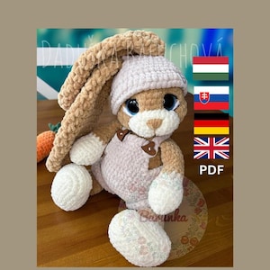 May include: A crocheted bunny rabbit toy with brown fur, a pink and white crocheted dress, and a pink crocheted hat. The bunny is sitting on a wooden surface. The image also includes the text "PDF" and flags for Hungary, Slovakia, Germany, and the United Kingdom.