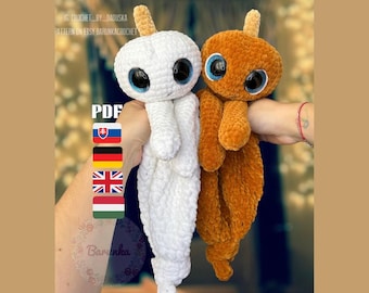 May include: Two crocheted amigurumi toys, one white and one brown, with large googly eyes and a horn on top of their heads. The toys are being held by a person's hands. The text "PDF" is visible in the image.
