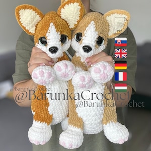 May include: Two handmade crochet corgi plushies. The corgis have brown and white fur, large black eyes, and pink paw pads. The plushies are held up in front of a person. The text "@BarunkaCrochet" is visible.