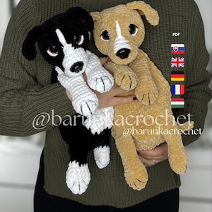Op de afbeelding: Twee gehaakte hondenspeeltjes van pluche. Eén is zwart en wit, de andere is bruin. Beide hebben witte poten en neuzen. De speeltjes worden vastgehouden voor een persoon die een groene trui draagt. De tekst "@barunkacrochet" is zichtbaar.
