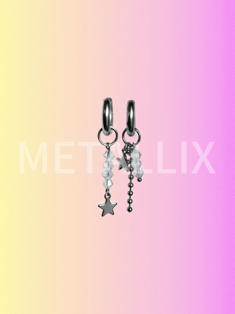 May include: A pair of silver hoop earrings with dangling charms. One earring features a star charm and clear beads, while the other has a cluster of stars and a chain of small beads. The word "METALIX" is visible in the image.