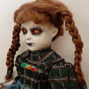 May include: A creepy porcelain doll with orange eyes and a plaid dress. The doll has long brown braids and a painted-on smile.