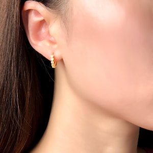 May include: A small gold hoop earring featuring a row of tiny, clear, round-cut stones set along the front edge. The earring is worn in the earlobe, showcasing a polished metallic finish and a secure, hinged closure mechanism for daily wear.