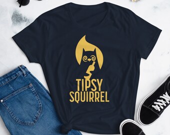 May include: Navy blue t-shirt with a gold graphic of a squirrel holding a wine bottle, with the text "TIPSY SQUIRREL". The shirt is paired with blue jeans and black sneakers.