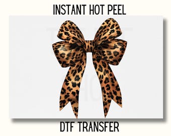 May include: A leopard print bow with a brown and black pattern. The bow is on a white background with the text "INSTANT HOT PEEL" and "DTF TRANSFER".