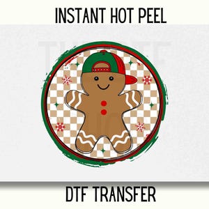 May include: A green, red, and white circle with a gingerbread man wearing a green and red hat. The gingerbread man is smiling and has two red buttons. The circle has a checkered pattern and snowflakes. The text "INSTANT HOT PEEL" is above the circle and "DTF TRANSFER" is below the circle.