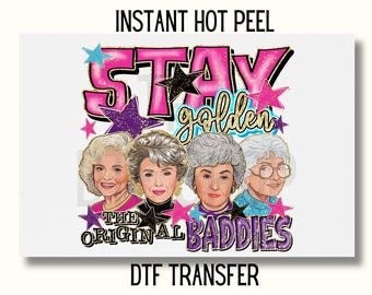 May include: A pink and gold graphic design with the text "Stay Golden" and "The Original Baddies". Four women with gray hair are pictured in the design. The design is on a white background.