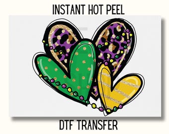 May include: Three overlapping hearts with a Mardi Gras theme. The hearts are green, purple, and gold with glitter and leopard print patterns. The hearts are decorated with purple and gold beads.