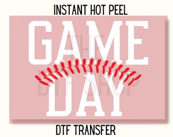 May include: A pink rectangular graphic with the words "GAME DAY" in large white letters. Below the words is a red design. The words "INSTANT HOT PEEL" and "DTF TRANSFER" are above and below the main text.