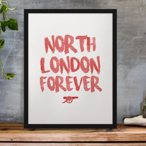 May include: A framed print with the words "North London Forever" in red watercolor lettering. The Arsenal Football Club crest is at the bottom of the print.