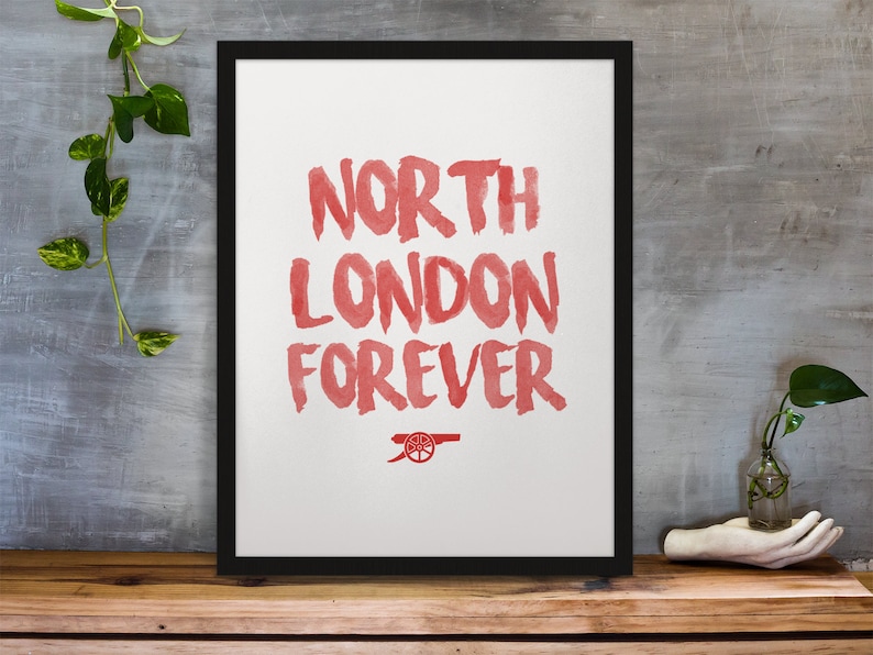 May include: A framed print with the words "North London Forever" in red watercolor lettering. The Arsenal Football Club crest is at the bottom of the print.