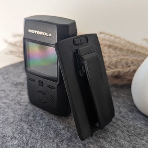 Könnte beinhalten: Ein schwarzes Motorola-Funkgerät mit einem Bildschirm, der ein Regenbogenmuster anzeigt. Das Funkgerät wird mit einem schwarzen Gürtelclip geliefert.