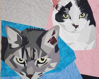May include: A geometric quilt depicting two cat faces. One cat is grey, the other black and white. The background includes blue, pink, and grey fabric. The cats have yellow eyes.