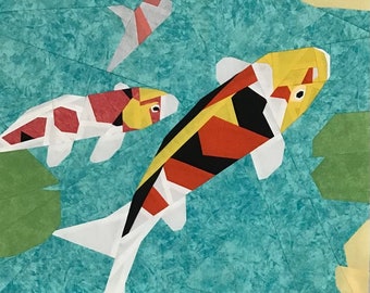 May include: A colorful quilt block featuring three koi fish swimming in a turquoise pond. The fish are red, yellow, black, and white. The pond is surrounded by green lily pads and white lily flowers.