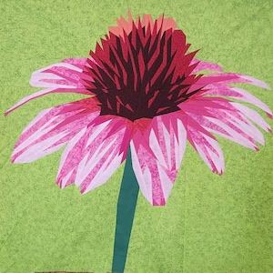 May include: A colorful, geometric fabric art piece featuring a large, stylized flower. The flower has pink and white petals, a dark red center, and a green stem against a light green background. The artwork is likely a quilt or fabric collage.