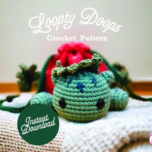 Può includere: Uno schema all'uncinetto per una creatura loopy dooms verde e rossa. Lo schema è disponibile per il download immediato. L'immagine mostra una creatura all'uncinetto con un cappello rosso e verde e un corpo verde.
