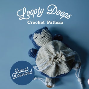 Könnte beinhalten: Ein gehäkeltes blaues und weißes Snorlax-Plüschtier mit einem Kordelzugbeutel-Design. Das Plüschtier liegt auf einem blauen Hintergrund mit dem Text "Loopty Doops Crochet Pattern" und "Instant Download" in Weiß.