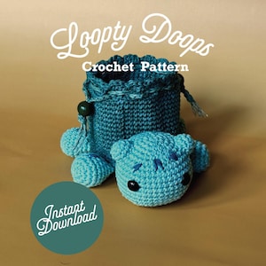Può includere: Un sacchetto per dadi all'uncinetto con uno schema di colori blu e verde. Il sacchetto ha la forma di una tartaruga con un viso carino. Il testo "Loopy Doops Crochet Pattern" è sopra il sacchetto. Il testo "Instant Download" è in un cerchio sotto il sacchetto.