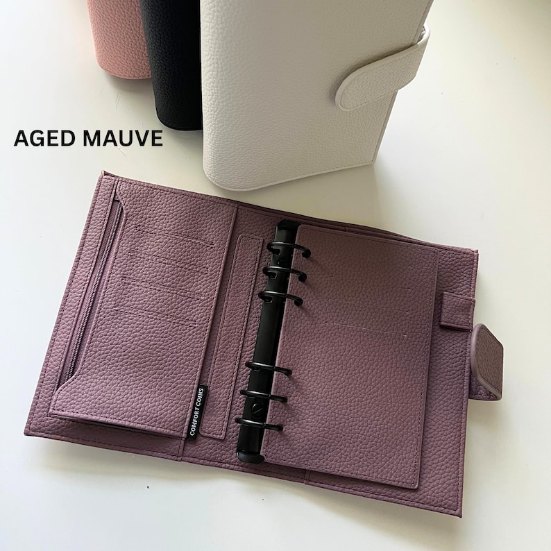 Op de afbeelding: Een open, verouderde mauvekleurige planner met een getextureerd oppervlak, zwarte ringbanden en meerdere binnenvakken. De planner is open, waardoor de binnenpagina's zichtbaar zijn. De tekst "AGED MAUVE" is zichtbaar.