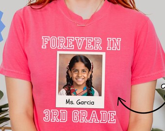 May include: A pink t-shirt with the words "FOREVER IN" above a photo of a girl and "3RD GRADE" below. The text "Ms. Garcia" is below the photo. The shirt also has the text "More Colors Available" and "Any Teacher Name".
