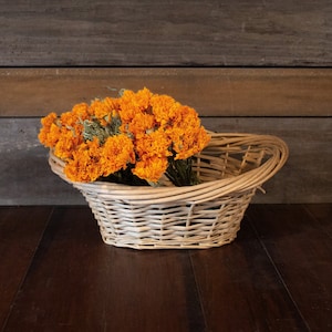 K&ouml;nnte beinhalten: Ein geflochtener Weidenkorb gef&uuml;llt mit leuchtend orangefarbenen Ringelblumen. Der Korb hat einen gebogenen Griff und steht auf einer dunklen Holzoberfl&auml;che und einem Hintergrund aus Holzplanken. Die Blumen sind in voller Bl&uuml;te.
