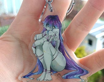 May include: A clear acrylic keychain featuring a seated anime-style character with long purple hair and teal skin. The character is wearing a purple outfit and has green eyes. The keychain has a silver chain.