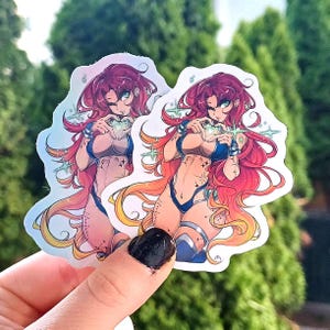 May include: Two holographic stickers featuring a stylized anime character with long red hair and a blue bikini. The character is holding a glowing green gem in a heart shape. The stickers have a shiny, iridescent finish.