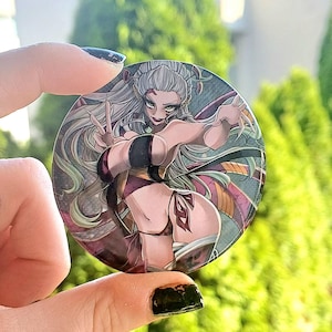 Könnte beinhalten: Ein runder Button mit einer detaillierten Anime-Illustration eines weiblichen Charakters mit langen weißen Haaren und grünen Augen. Der Charakter trägt ein Outfit in Schwarz und Burgunder. Der Hintergrund ist eine Mischung aus Farben. Der Button wird gehalten.