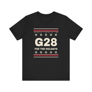 May include: A black short-sleeved t-shirt featuring a graphic print with the text G28 FOR THE HOLIDAYS. The design includes red and white geometric patterns, snowflake icons, and technical code text G91 G28 Z0. G28 X0. Y0. M30.