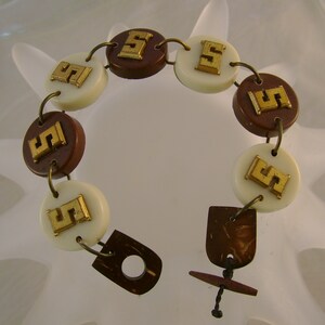 May include: A brown and white bracelet with gold-colored letter 'S' charms. The bracelet is made of round beads and has a brown wooden toggle clasp.