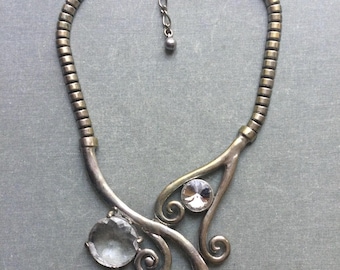 Puede incluir: Un collar de tono plateado con una cadena y un colgante con un diseño de espiral con tres piedras de cristal transparentes.