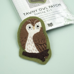 May include: A Tawny Owl Patch sewing kit featuring a felt owl applique in shades of brown, white, and dark brown, perched on a dark brown branch against a light green background. The packaging includes the text Tawny Owl Patch Sewing Kit.