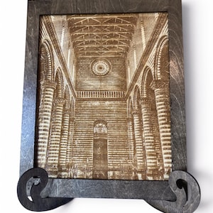May include: A rectangular dark wood frame containing a laser-engraved sepia-toned image of a cathedral interior with tall columns, arched ceilings, and a circular rose window. The frame features two decorative scroll-shaped feet at the bottom.