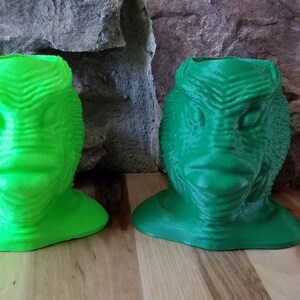 May include: Two green 3D printed creature head planters. The planters are shaped like the head of a creature from the black lagoon.