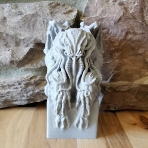 May include: A gray 3D printed sculpture of a Cthulhu-like creature with tentacles and a gaping mouth. The sculpture is on a gray base.