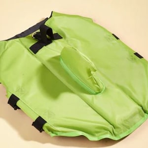 May include: A bright green dog life jacket with black straps and a handle. The jacket has a built-in flotation device and a safety buckle.