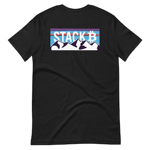 Puede incluir: Camiseta negra con un gráfico rectangular en la espalda. El gráfico presenta el texto "STACK B" sobre un diseño de cordillera. Las montañas son blancas, con un cielo azul y acentos morados y naranjas.