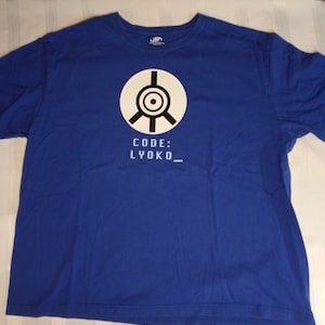 Puede incluir: Una camiseta azul real con un círculo blanco que contiene un diseño de ojo estilizado negro y el texto "CODE: LYOKO_" en blanco.
