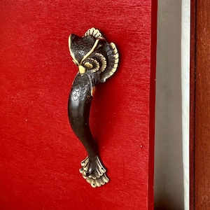 Könnte beinhalten: Auf einer leuchtend roten Tür montierter Türgriff aus Bronze in Form einer Eule. Der Griff weist detaillierte Feder- und Flügeldesigns mit goldenen Akzenten auf und verleiht dem Eingang einen Hauch von Eleganz.