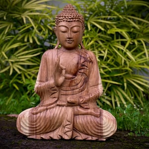 May include: A wooden statue of Buddha sitting in a meditative pose with his right hand raised in a gesture of blessing. The statue is carved from a light brown wood and has a detailed face with a serene expression.