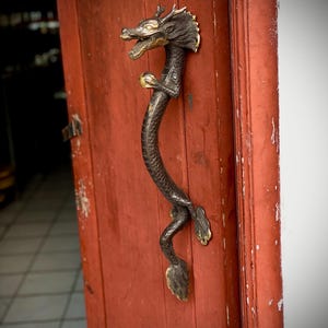 Peut inclure: Une poignée de porte en forme de dragon noir avec des accents dorés sur une porte en bois rouge.
