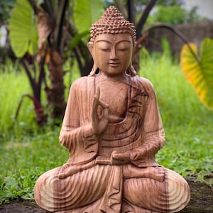 May include: A wooden statue of Buddha sitting in a meditative pose with hands in the Dhyana mudra. The statue is carved with intricate details and has a warm brown color.